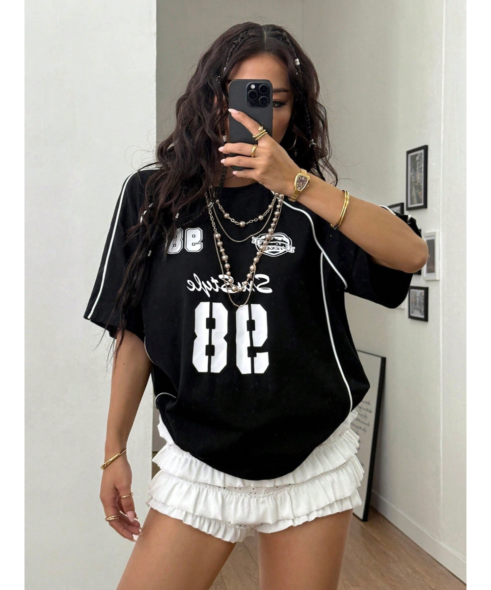 Woman wearing a black oversized t-shirt with white text and numbers, paired with a white skirt, taking a mirror selfie.